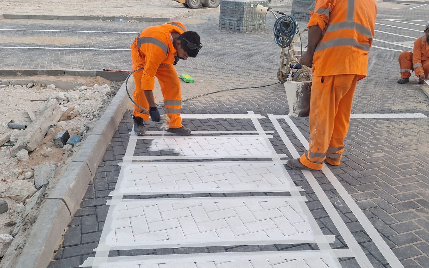 Marking crew spraying a masked pedestrian crossing onto interlock paving